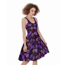 Load image into Gallery viewer, A woman modeling a sleeveless fit-and-flare dress with a Halloween print of purple pumpkins, orange jack-o'-lanterns, and purple flowers on a black background, set against a plain white studio backdrop.