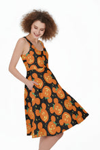 Load image into Gallery viewer, A woman modeling a sleeveless A-line dress with a black background and an all-over orange jack-o'-lantern pattern, posed against a plain white studio background.
