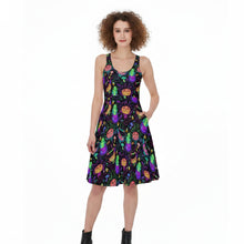 Load image into Gallery viewer, A woman modeling a sleeveless A-line dress with a black background and a colorful print of cartoonish green and purple gourds with orange faces. She is wearing black ankle boots against a plain white studio background.

